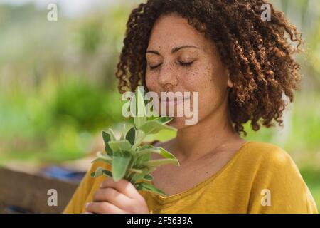 Woman with eyes closed smelling sage in garden Stock Photo