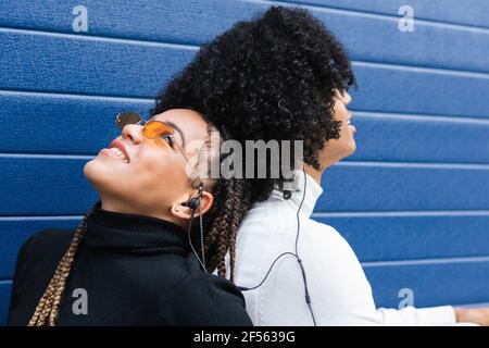 Smiling girlfriend leaning on boyfriend while sitting against blue wall Stock Photo