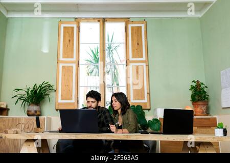 Male and female design professionals working on laptop at desk in industry Stock Photo