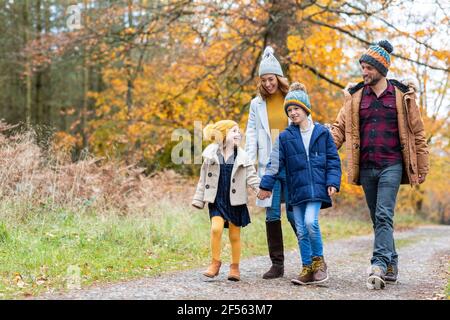 Siblings holding hands while walking with parents on forest path Stock Photo