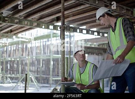 Male construction workers holding digital tablet while planning with coworker at construction site Stock Photo