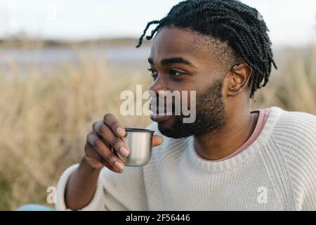 Smiling young man drinking tea while looking away Stock Photo