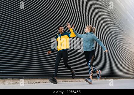 Male and female sportsperson doing high-five while running on sidewalk during sports training by wall Stock Photo