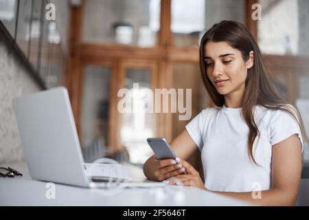 Young happy woman using a smart cell phone to look at her selfies to pick a new social media profile picture. Stock Photo