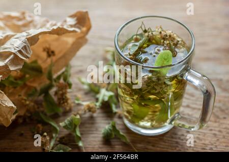 Fresh lime tea by dried linden leaves in paper bag on wooden cutting board Stock Photo