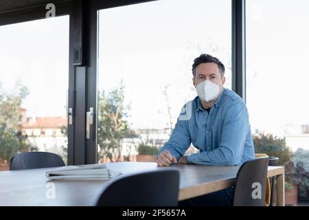 Mature man wearing protective face mask sitting at home Stock Photo