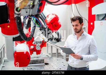 Young man using digital tablet by robotics in factory Stock Photo