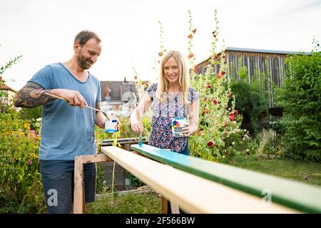 Cheerful couple painting wooden plank in garden Stock Photo