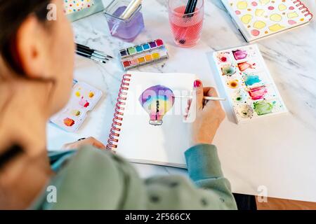 Woman painting light bulb with watercolors on spiral notebook Stock Photo