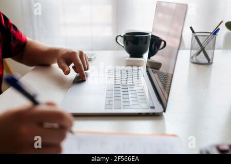 Man writing while using laptop on table at home office Stock Photo