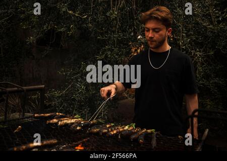 Young man preparing Calcots on barbecue while standing at backyard Stock Photo