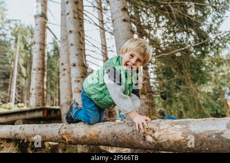 Playful boy crawling on log in forest at Salzburger Land, Austria
