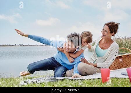 Daughter and father having fun while sitting by mother on blanket by lake Stock Photo