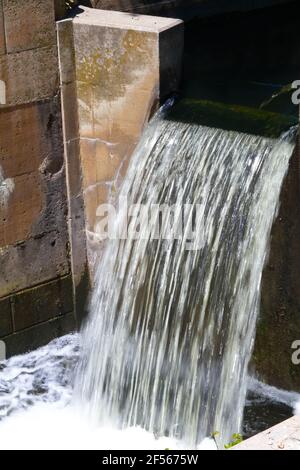 Vertical view of water flowing through a channel on the canal creating a foaming slurry at the base of the falls Stock Photo