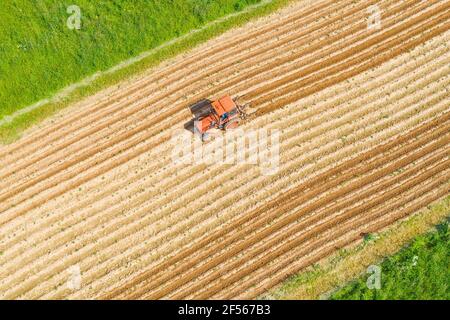 Rural landscape aerial view of a village on a field with plantings of vegetable crops, plowing hilling the soil in rows using agricultural machinery a Stock Photo