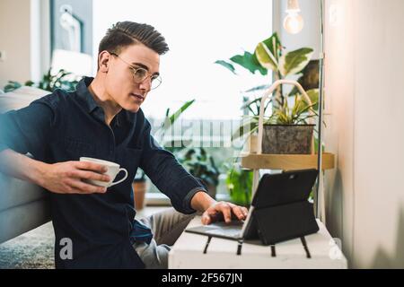 Young man in eyeglasses using laptop while sitting in living room Stock Photo