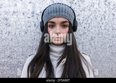Beautiful teenage girl with long hair listening music through headphones against silver wall Stock Photo