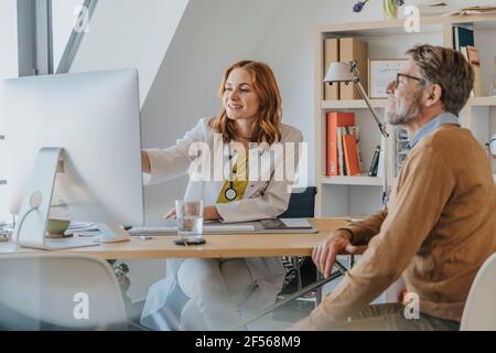 General practitioner using computer while sitting by patient at doctor's office Stock Photo