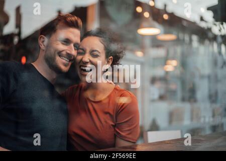Happy couple laughing while sitting by table at cafe Stock Photo