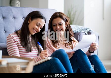 Smiling mother and daughter checking bills while sitting by sofa in living room Stock Photo
