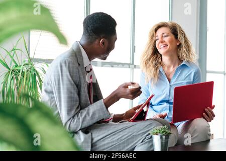 Smiling professional colleagues talking to each other with digital tablet and laptop while sitting Stock Photo
