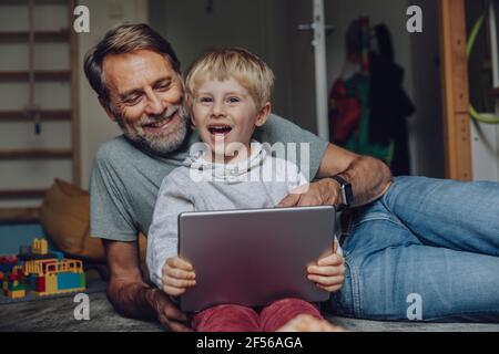 Smiling father and son using tablet in bedroom Stock Photo