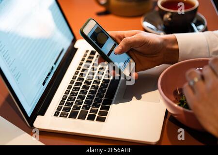 Businessman using smart phone over laptop while sitting at cafe Stock Photo