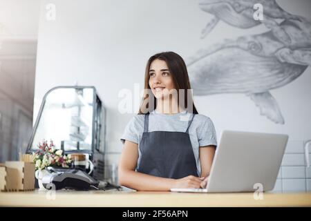 Portrait of woman barista having a short rest from her work at busy cafe enjoying the sunlight using a laptop. Stock Photo