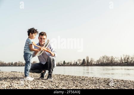 Young man and boy checking airplane toy by lake Stock Photo