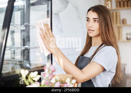 Portrait of young cafe owner lady using wipe to clean everything before opening. Stock Photo
