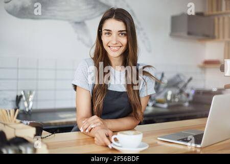 Small coffee shop owner happy to run her business looking at camera smiling and drinking coffee. Stock Photo