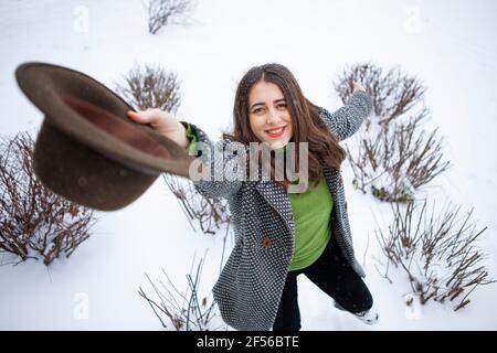 Smiling beautiful woman holding hat while standing in snow during winter Stock Photo