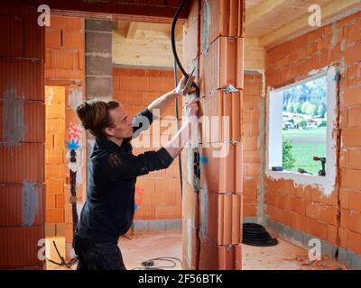 Male electrician installing cables between bricks while working at construction site Stock Photo