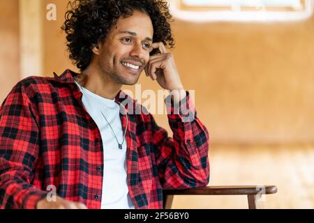 Smiling man looking away while sitting at spacious room Stock Photo