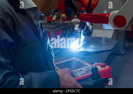 Worker operating control by robotic arm welding in industry Stock Photo