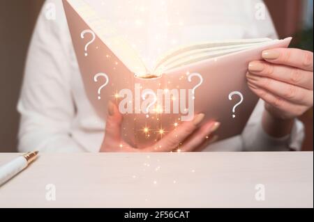 Female hands holding open book with question marks. Education concept. Stock Photo