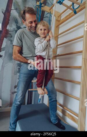 Happy father assisting son climbing rope in living room Stock Photo