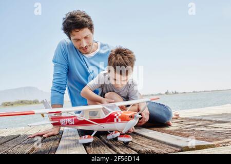 Boy checking toy airplane while sitting on pier Stock Photo