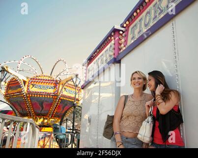 Smiling female friends talking while standing against ticket counter at amusement park Stock Photo