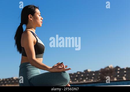Young female athlete meditating while practicing lotus position on sunny day Stock Photo