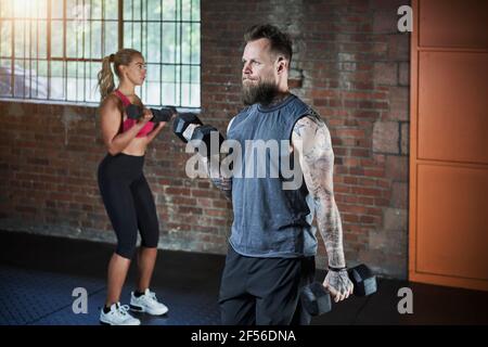 Female and male athlete exercising with dumbbells in gym Stock Photo