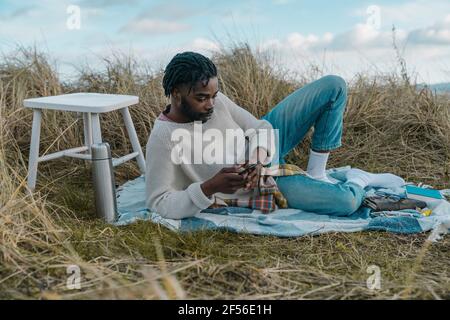 Young man using mobile while lying on blanket at beach Stock Photo