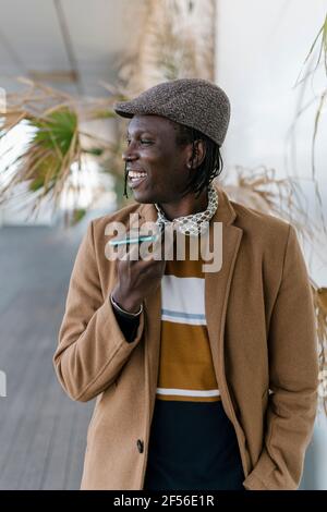 Smiling man in flat cap talking on smart phone through speaker Stock Photo