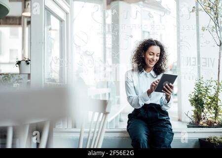 Smiling young businesswoman using digital tablet while sitting at cafe Stock Photo