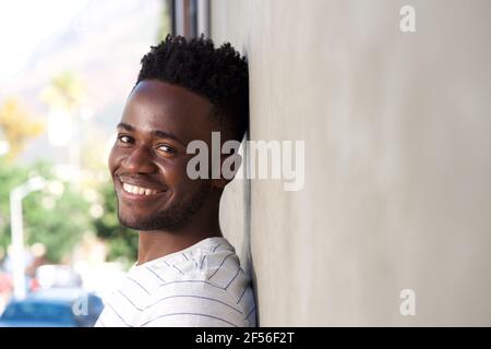 Close up side portrait of smiling handsome man leaning on wall outside Stock Photo