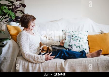 Senior woman using laptop while sitting on sofa with Jack Russell Terrier at home Stock Photo