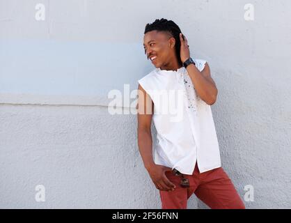 Portrait of young man with dreadlocks smiling outside against gray wall Stock Photo