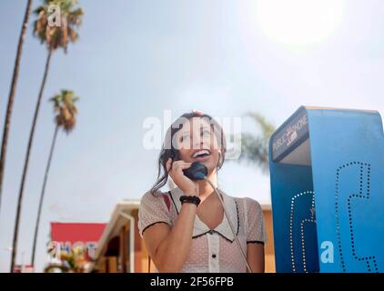 Young woman talking on pay phone while standing against sky Stock Photo