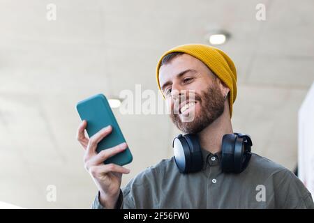 Smiling man with knit hat using smart phone while standing outdoors Stock Photo