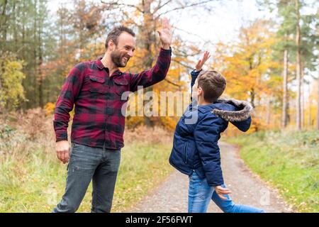 Smiling man giving high-five to boy while standing at forest Stock Photo